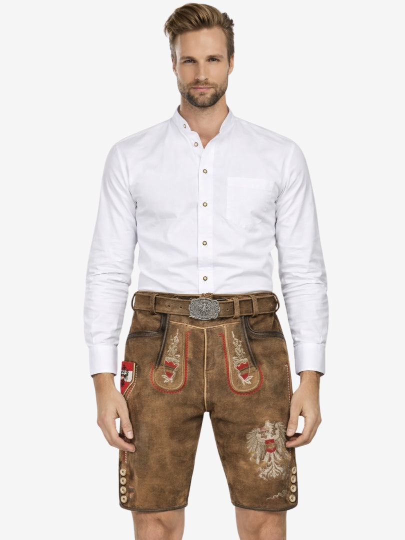 Front view of a man wearing brown lederhosen with red and white embroidery, paired with a white shirt and decorative belt.
