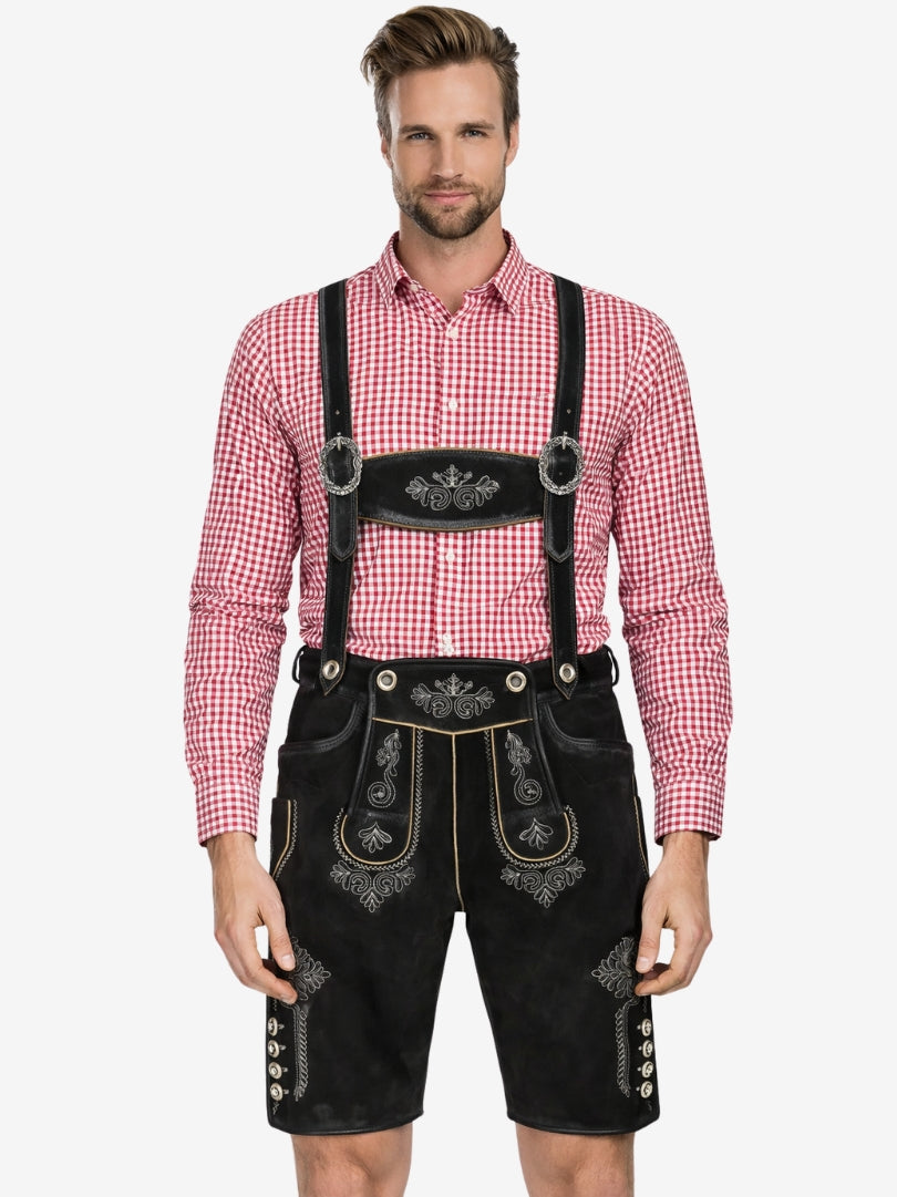 Man wearing black embroidered lederhosen with suspenders and a red checkered shirt, standing against a plain background.