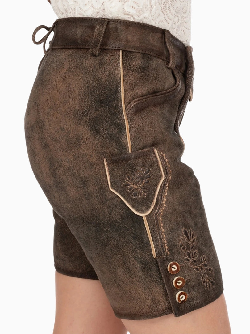 Side view of dark brown traditional lederhosen-style shorts with embroidered detailing, contrast piping, small side pocket, and decorative buttons on the leg, worn with a white lace top.