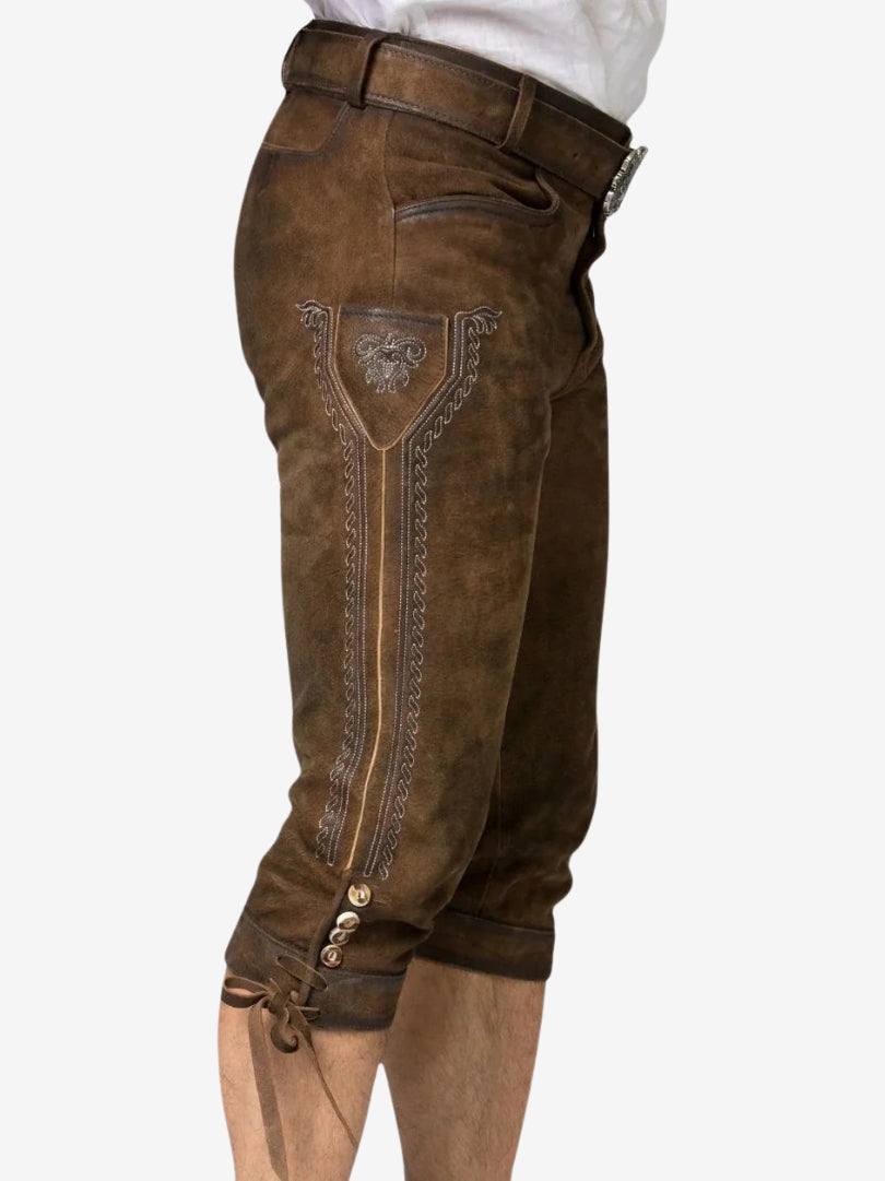 Side view of brown leather bundhosen showing decorative embroidery panel, belt loops, and knee button details with tie.