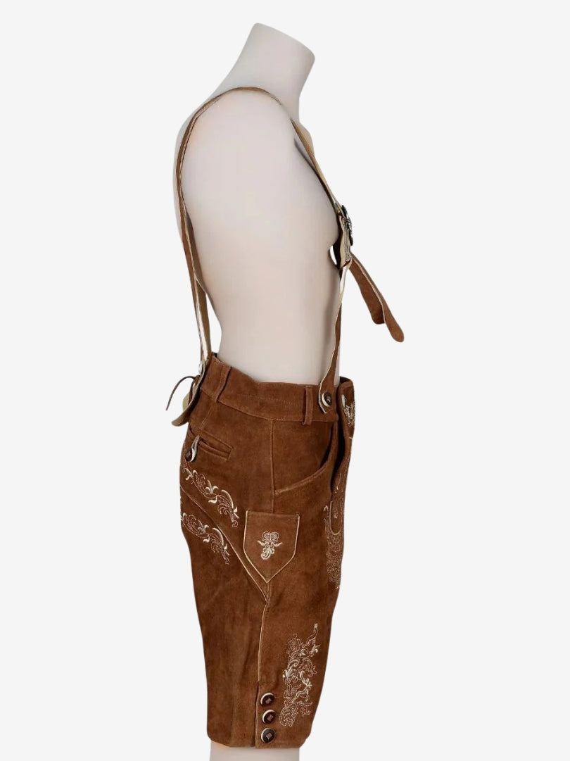Side view of brown suede lederhosen with suspenders on a mannequin, showing floral embroidery and side button details.