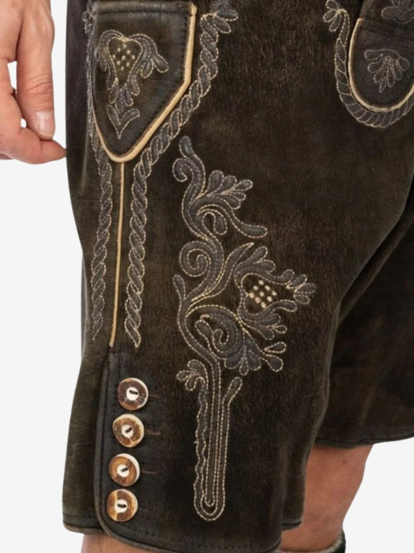 Close-up of dark brown lederhosen showing intricate embroidery on the thigh, decorative stitching, and traditional horn-style buttons on the side.