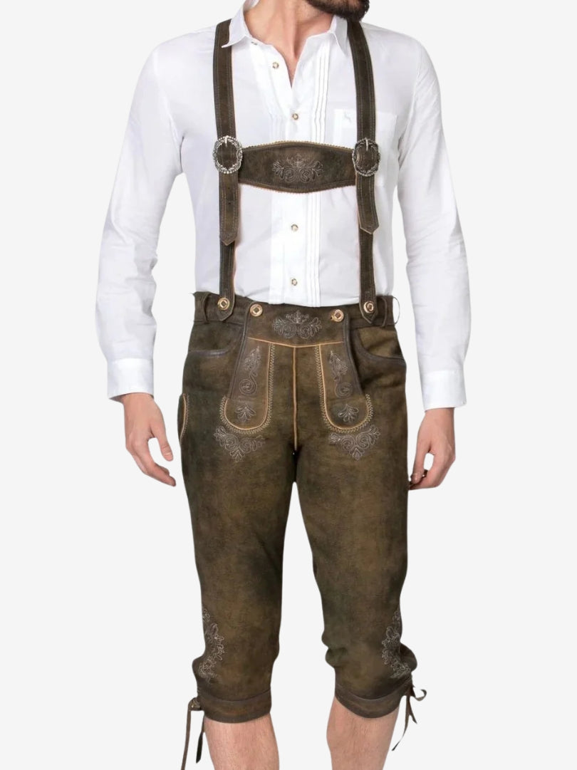 Man wearing brown leather bundhosen with suspenders and white shirt, featuring traditional embroidery on the front flap and thighs.