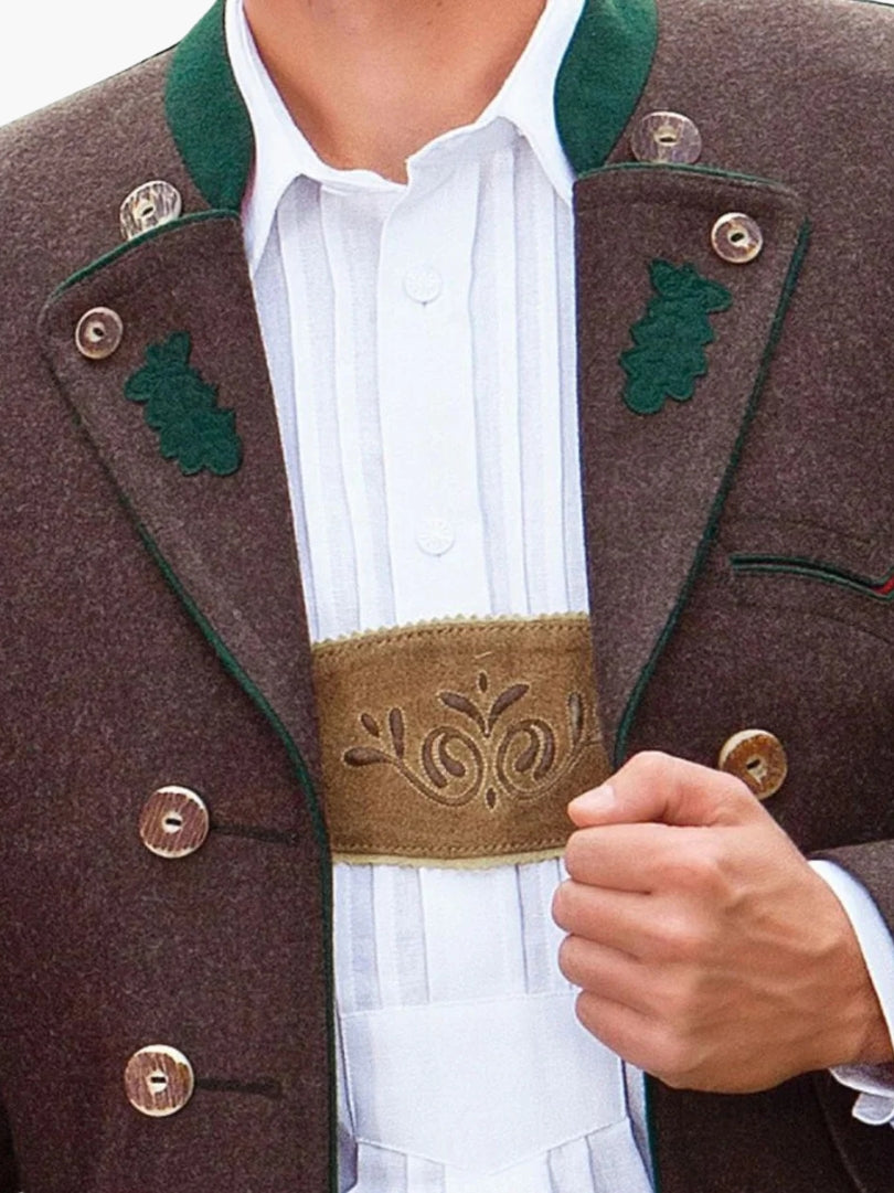 Close-up of brown Trachten jacket showing decorative buttons, green embroidered lapels, and embroidered chest panel over a white shirt.