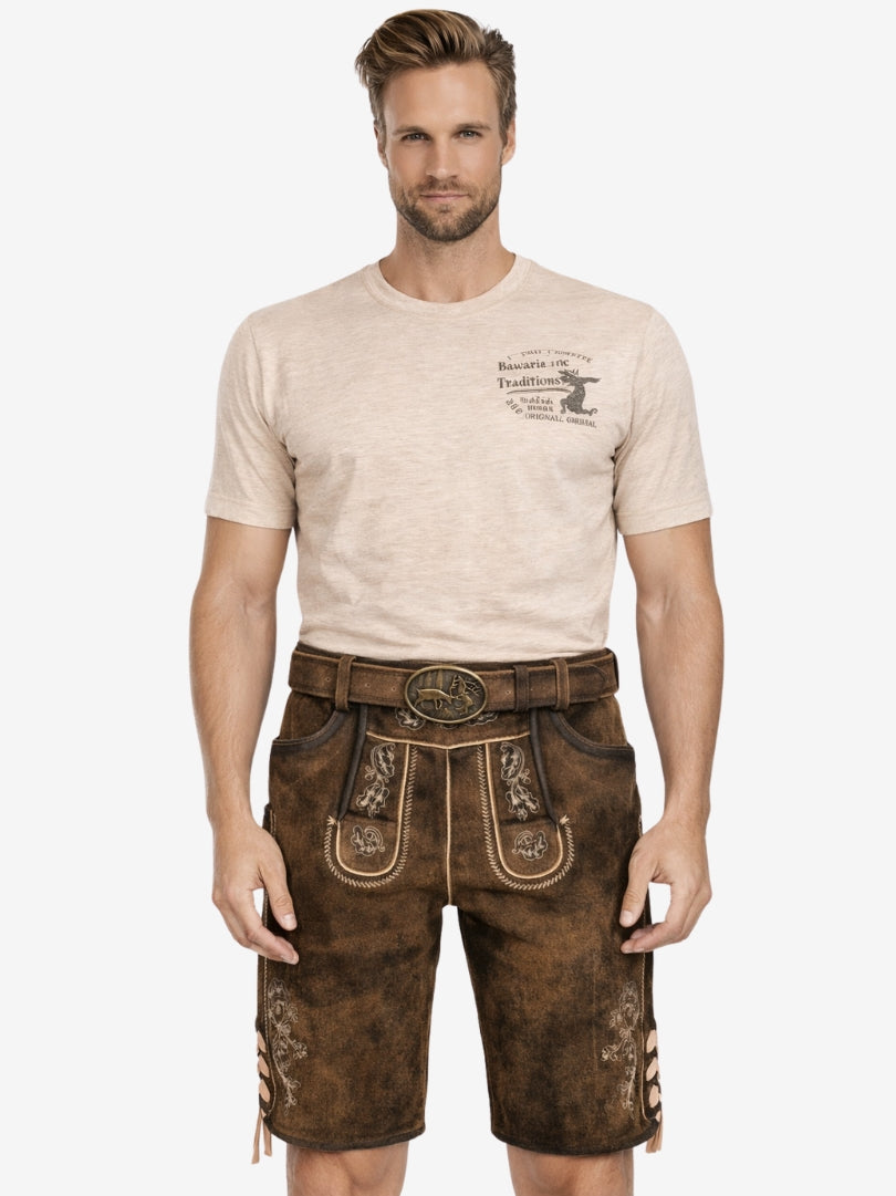 Man wearing rustic brown leather lederhosen with embroidered detailing, paired with a beige T-shirt and a traditional belt featuring a deer buckle.