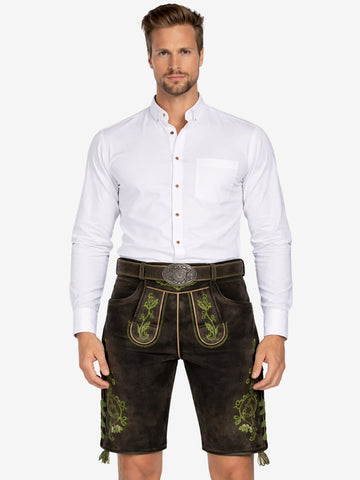 A man wearing traditional brown leather lederhosen with green embroidery, paired with a white button-up shirt, standing against a plain background.