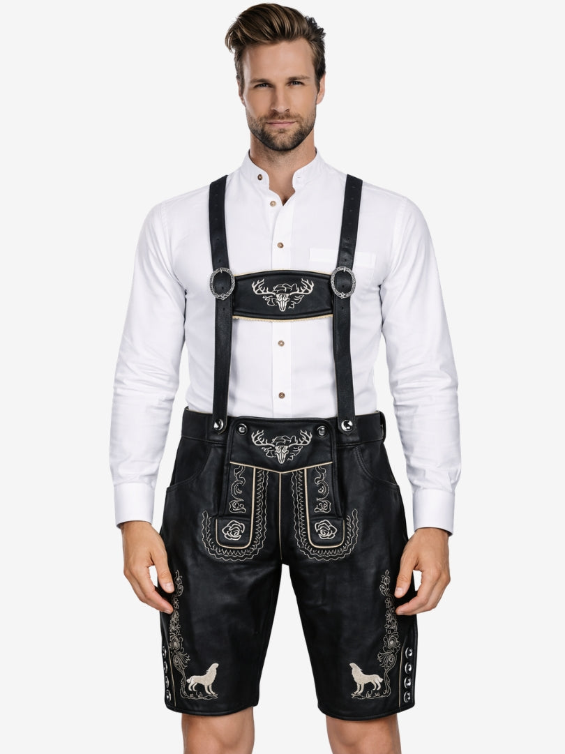 Man wearing black leather lederhosen with suspenders, featuring white embroidery and stag head motif, paired with a white shirt.