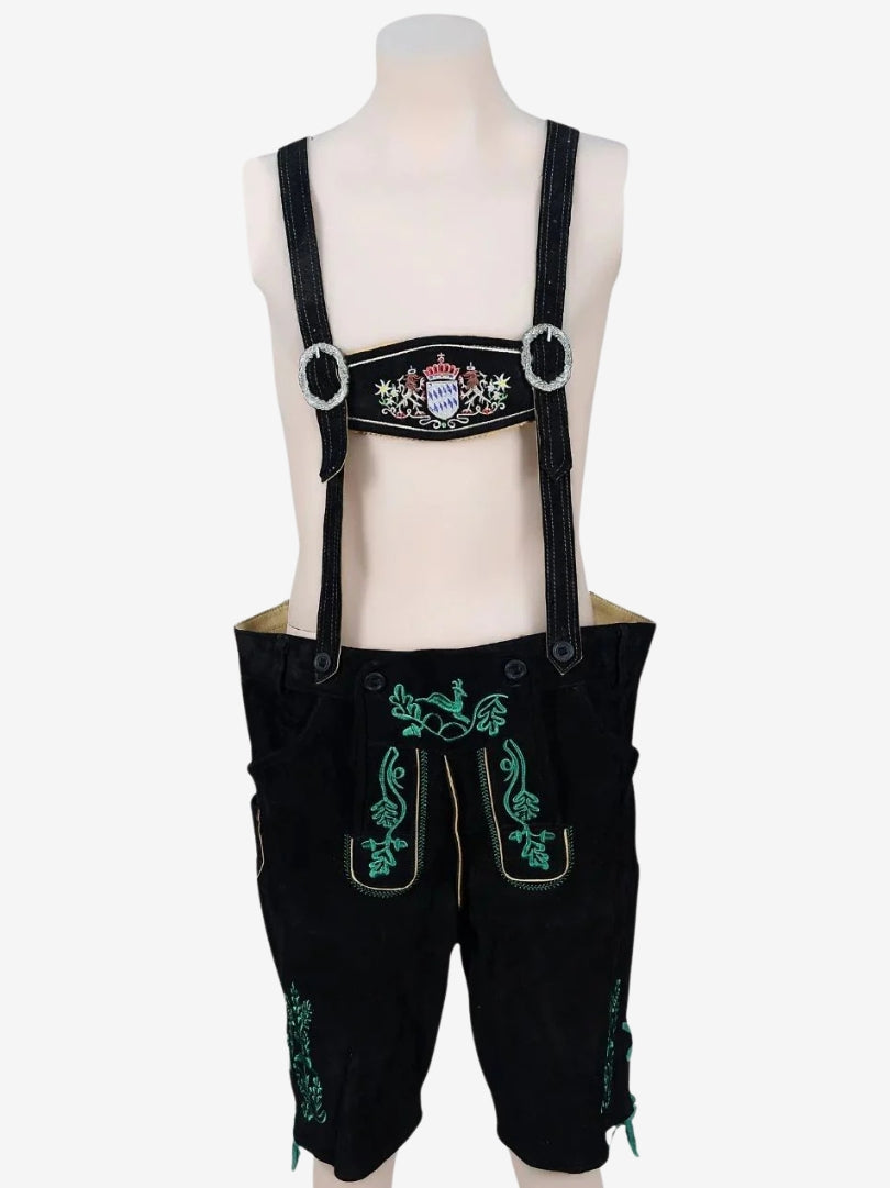 Black lederhosen with suspenders displayed on a mannequin, showing decorative front panel and green embroidered details.