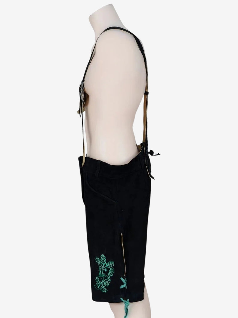 Side view of black lederhosen with green embroidery, highlighting lace-up leg opening and stitched patterns.