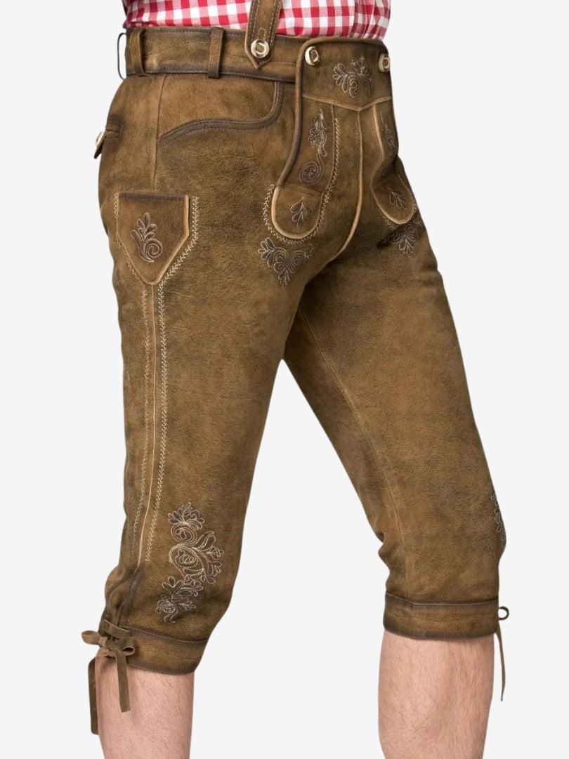 Close-up side view of brown leather bundhosen showing embroidered front flap, side pocket detail, and knee ties.
