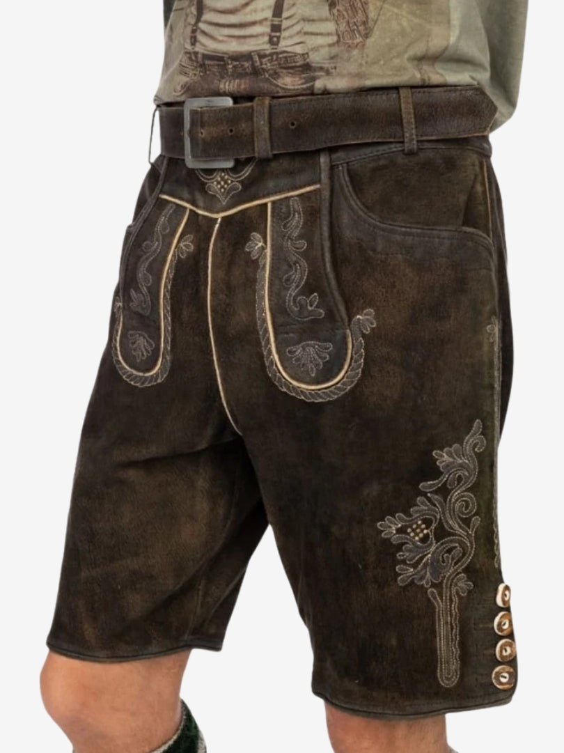 Man wearing dark brown leather lederhosen with detailed embroidery and a belt, paired with a casual t-shirt.