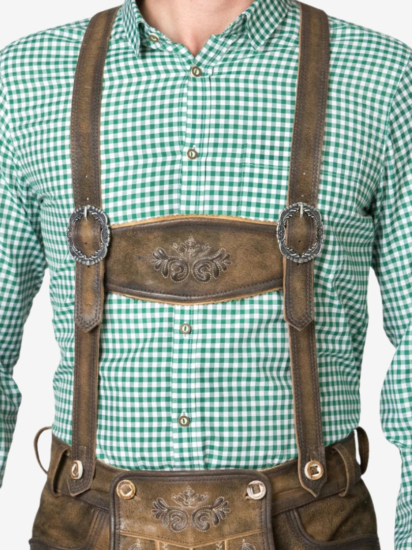 Close-up of lederhosen suspenders and chest panel with embossed detailing, worn over a green gingham shirt.