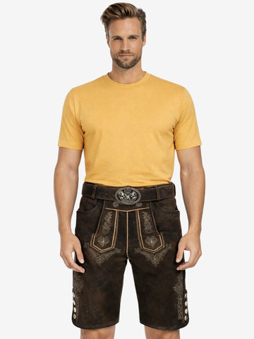 Man wearing dark brown embroidered lederhosen with a yellow T-shirt and traditional belt featuring a decorative buckle.