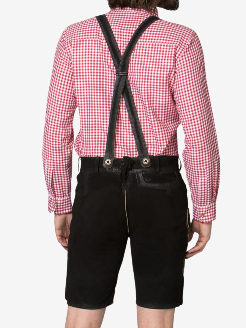 Rear view of a man wearing black lederhosen with suspenders crossed at the back and a red checkered shirt.