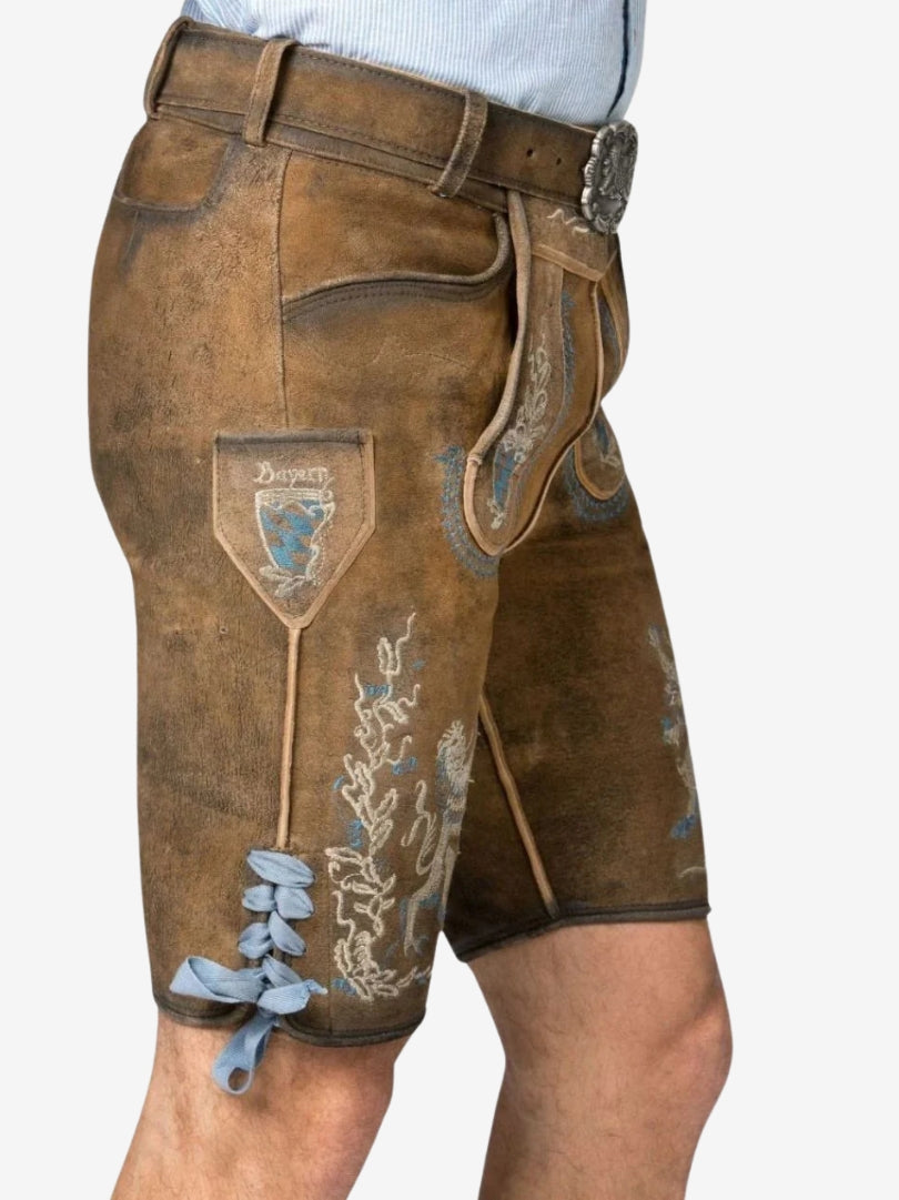 Side view of lederhosen showing embroidered Bavarian crest, lion design, side pocket, and blue ribbon lacing near the hem.