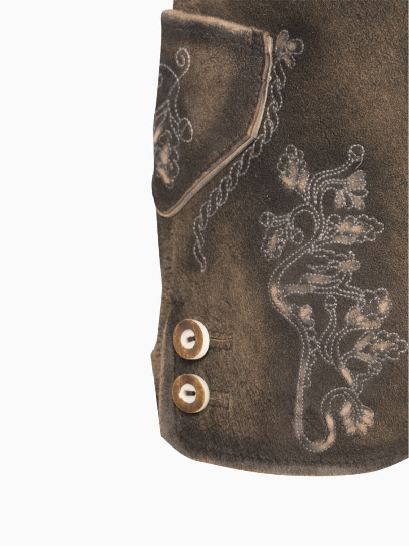 Close-up side view of rustic brown traditional lederhosen-style shorts showing embroidered floral detailing and decorative buttons near the hem on a textured leather finish