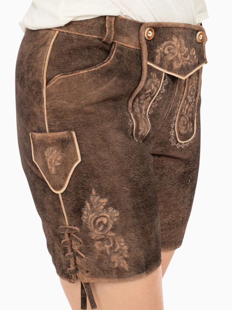 Angled front view of dark brown traditional lederhosen style shorts with embroidered patterns, decorative front flap with buttons, side pocket detail, and a distressed leather texture.