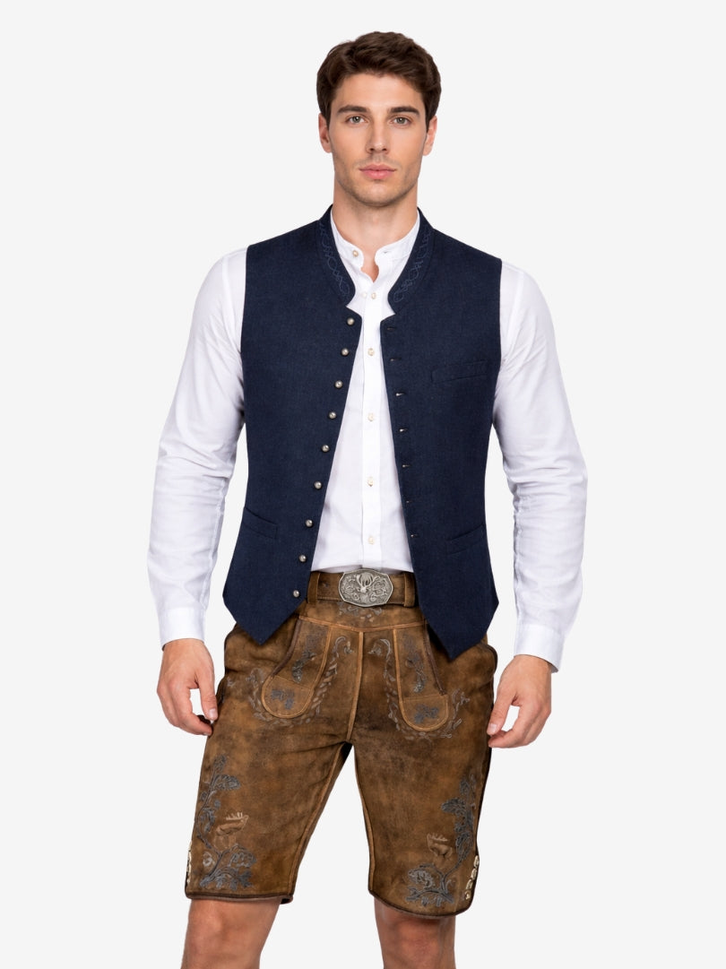 Man wearing brown lederhosen with blue embroidered details, paired with a white shirt, navy vest, and traditional belt with metal buckle.