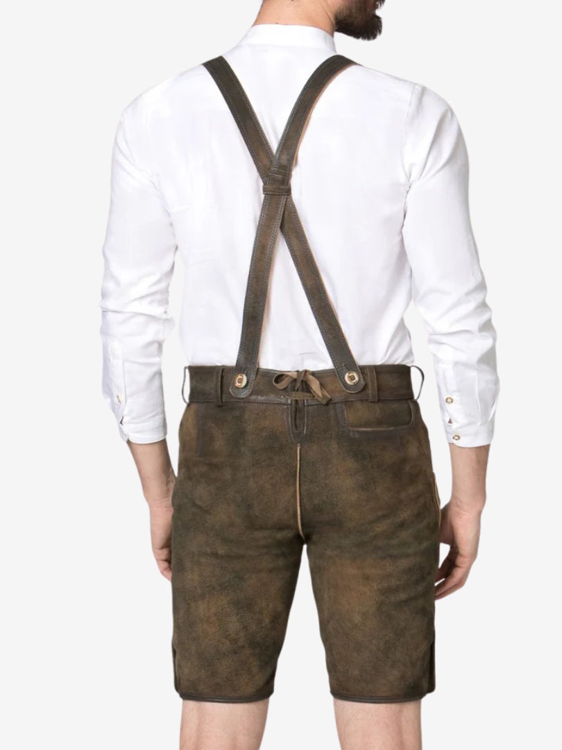 Back view of man wearing brown leather lederhosen with crossed suspenders and white shirt.