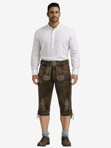 Man wearing dark brown leather bundhosen with a white shirt, socks, and shoes in a full-length front view.