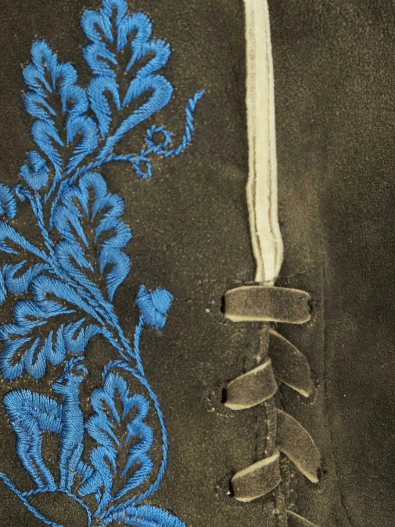 Close-up of side lacing on lederhosen with blue floral embroidery and suede tie closures.