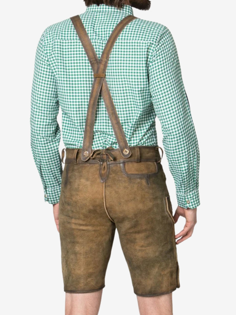 Rear view of a man wearing light brown lederhosen with crossed suspenders and a green checkered shirt.