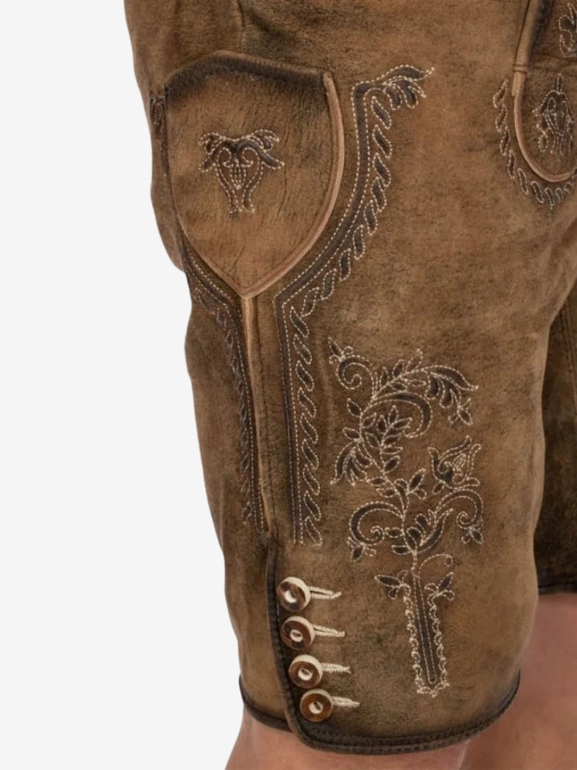 Close-up of intricate floral embroidery and button accents on the thigh of tan lederhosen.