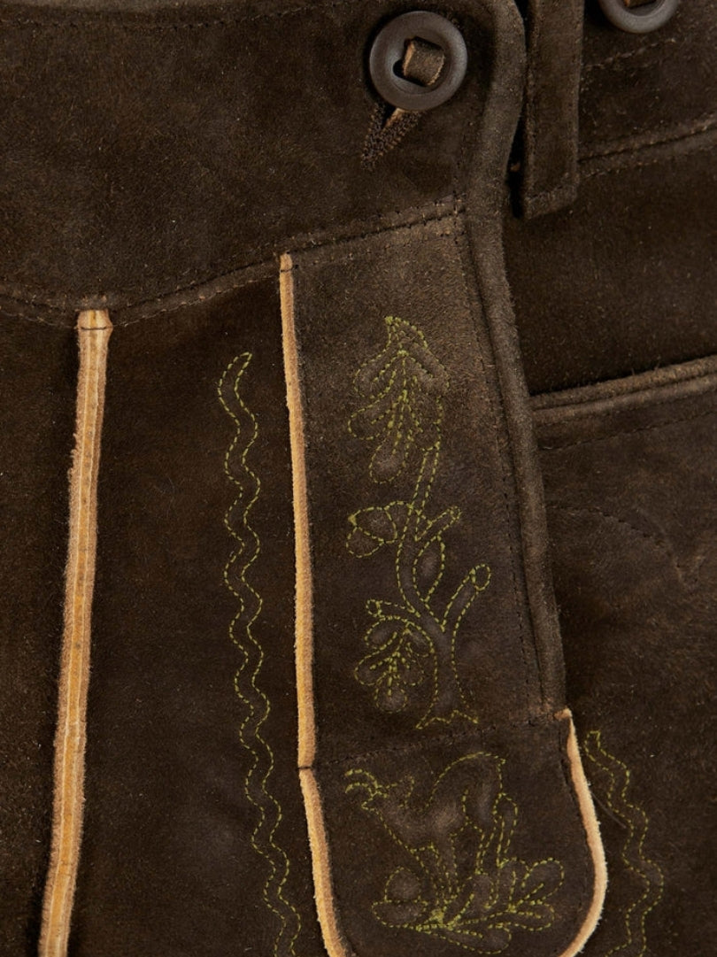 Close-up of front flap panel showing fine green embroidery, contrast piping, and traditional stitching on leather lederhosen.