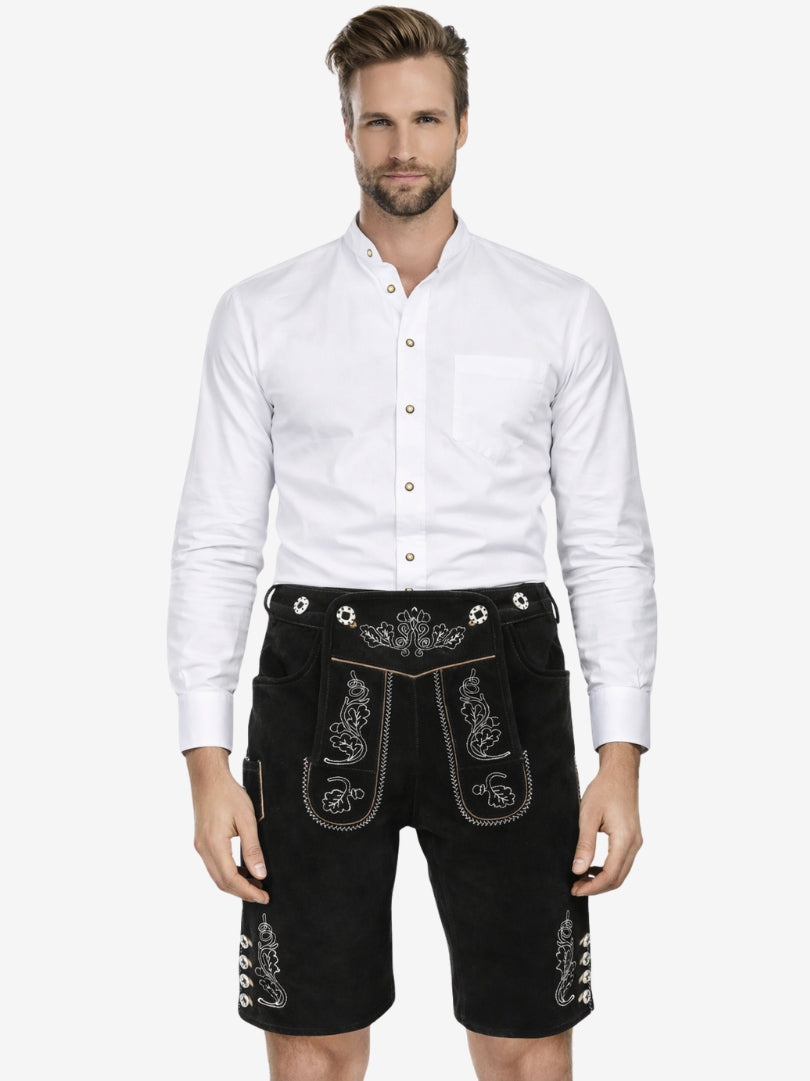 Man wearing a white button-up shirt paired with black embroidered lederhosen shorts, standing against a plain background.