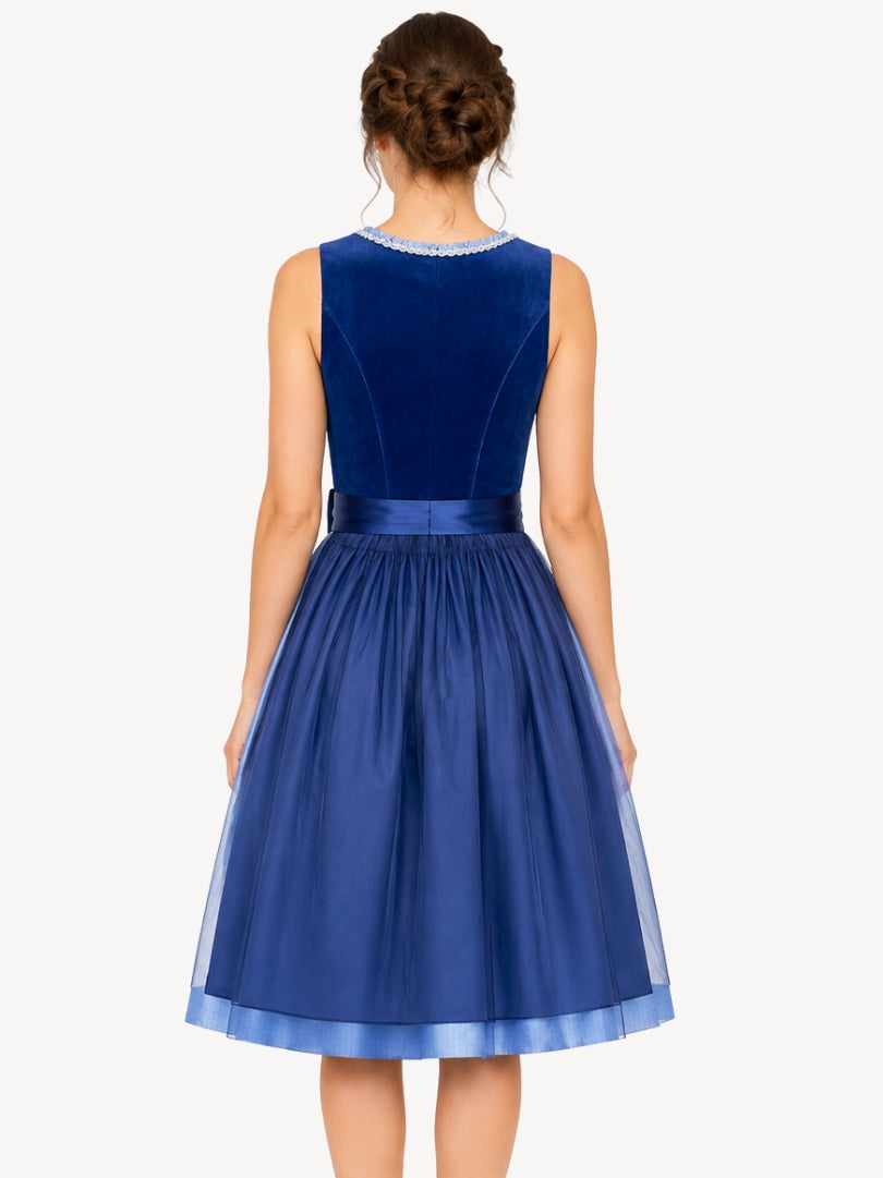 A woman shown from the back wearing a sleeveless royal blue dress with a velvet back panel, a matching satin waistband, and a pleated tulle skirt on a light gray studio background.