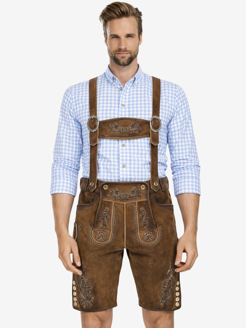 Man wearing brown embroidered lederhosen with suspenders and a light blue checkered shirt, standing against a plain background.