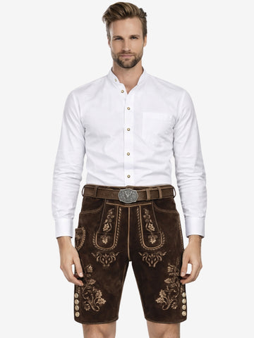 Man wearing a white button-up shirt paired with dark brown embroidered lederhosen and a traditional belt, standing against a plain background.