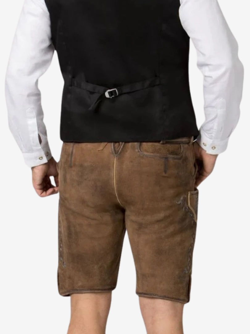 Back view of brown suede lederhosen shorts with subtle blue embroidery, worn with a white shirt and dark vest.