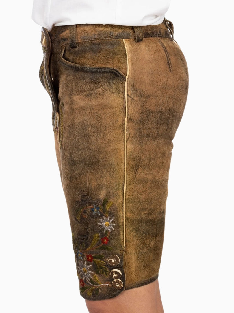 Side view of rustic brown traditional lederhosen-style shorts with floral embroidery, contrast piping, and decorative buttons near the hem, showing a worn leather texture.