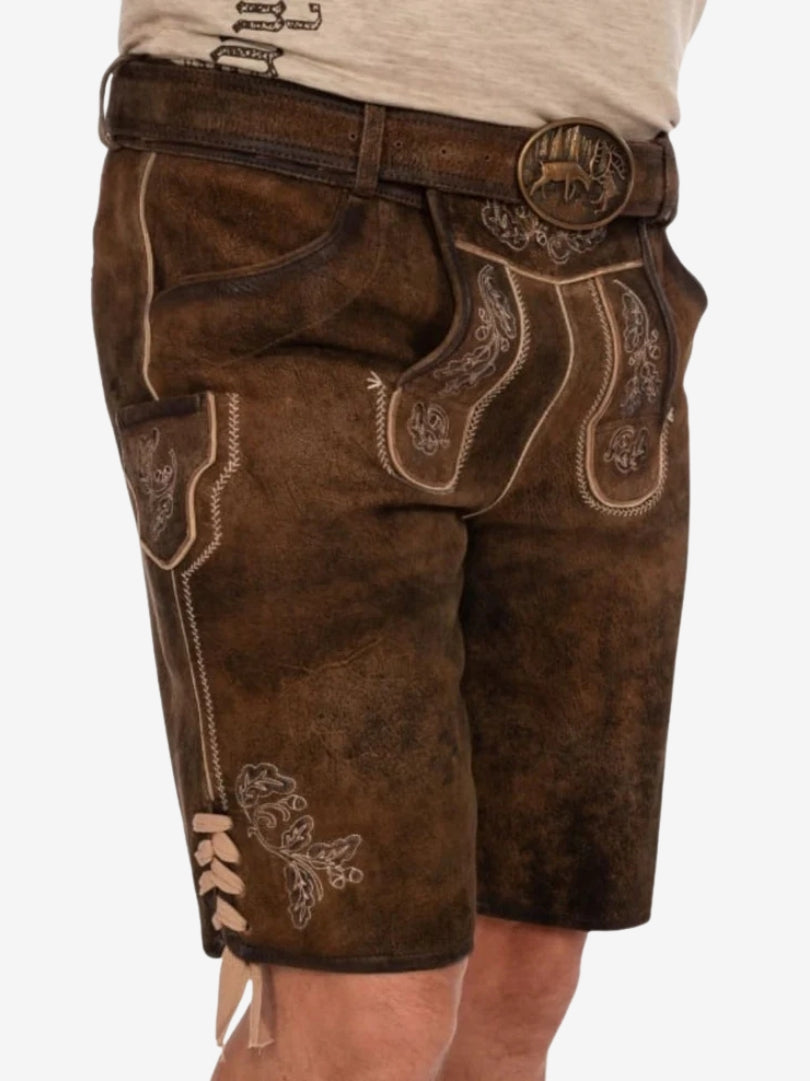 Angled side view of brown lederhosen highlighting front flap embroidery, side pocket, and lace-up detailing on the thigh.