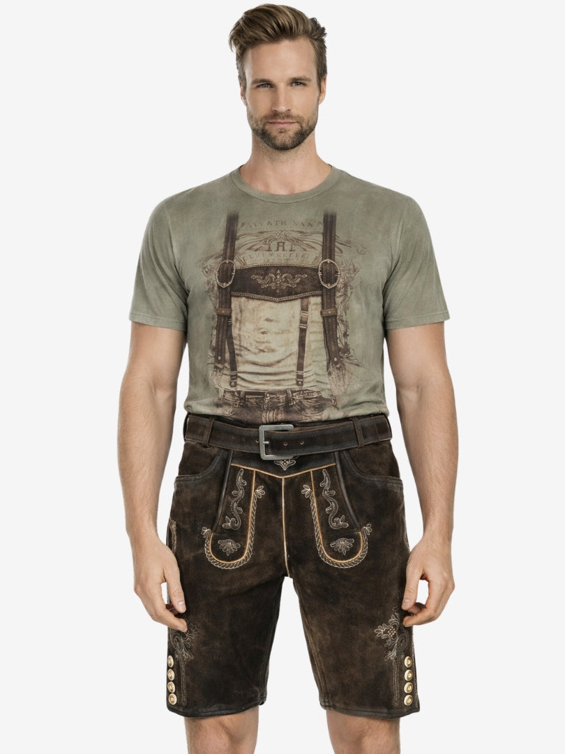 Man wearing dark brown embroidered lederhosen with a printed t-shirt, standing against a plain background.