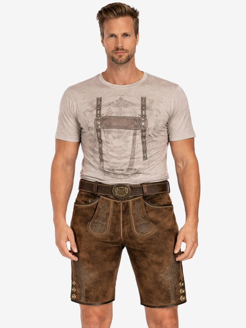 Man wearing brown embroidered lederhosen with a beige printed t-shirt and belt, standing against a plain background.