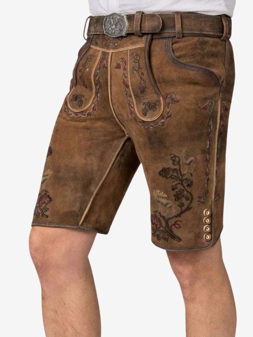 Angled view of brown lederhosen with intricate embroidery, front flap detailing, and textured suede material.