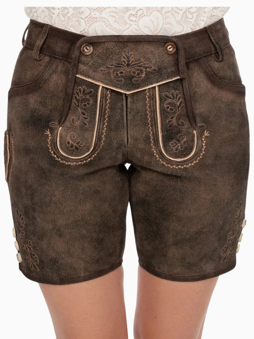 Front view of dark brown traditional lederhosen-style shorts featuring embroidered patterns, decorative front flap with buttons, and a distressed leather texture, worn with a white lace top.