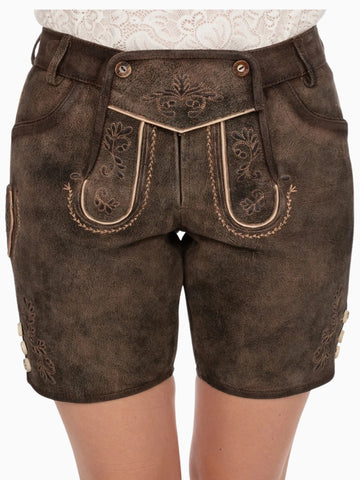 Front view of dark brown traditional lederhosen-style shorts featuring embroidered patterns, decorative front flap with buttons, and a distressed leather texture, worn with a white lace top.