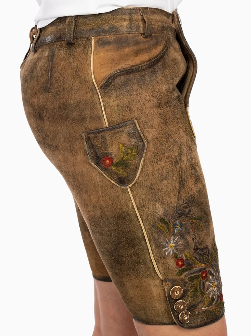 Front view of rustic brown traditional lederhosen-style shorts featuring colorful floral embroidery, decorative front flap with buttons, and a textured leather finish.