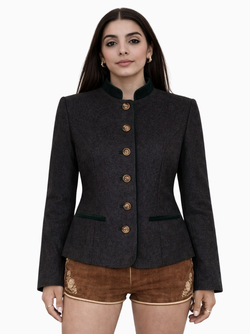 Front view of a women’s charcoal grey Bavarian Trachten jacket with dark green velvet stand collar, decorative metal buttons, tailored waist fit, and traditional brown embroidered lederhosen shorts, reflecting classic Alpine heritage style.