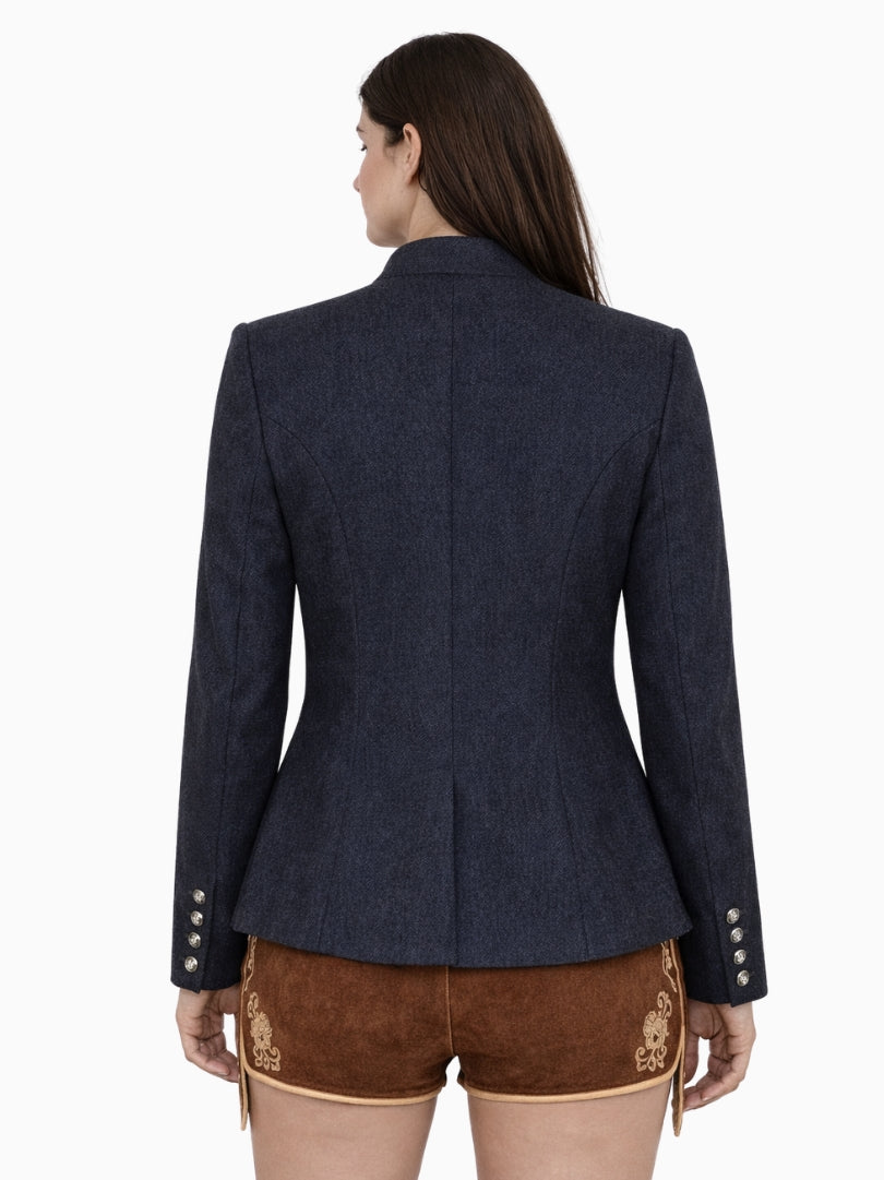 Back view of women’s navy blue Bavarian Trachten jacket with tailored fit, long sleeves, and traditional Alpine design paired with embroidered brown lederhosen shorts.