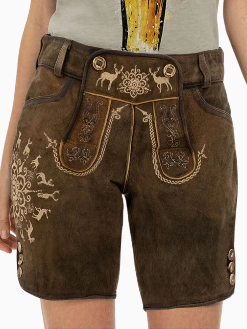 Close-up of a person wearing traditional brown Bavarian lederhosen made of leather, featuring decorative embroidery with deer and floral patterns, front flap detailing, and side buttons, paired with a light-colored shirt.