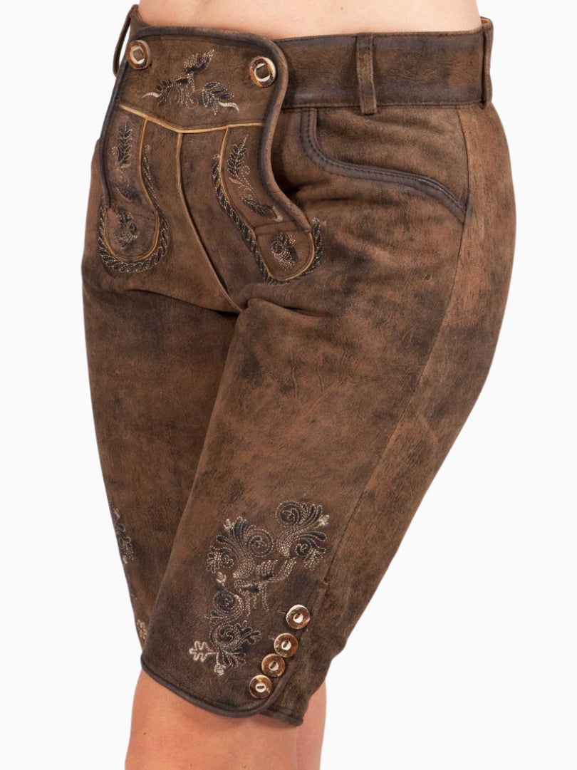 Close-up front view of rustic brown traditional lederhosen-style shorts featuring embroidered patterns on the decorative front flap and contrast piping details.