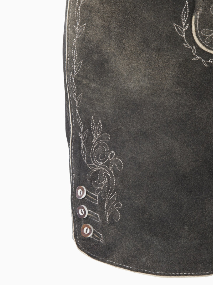 Close-up side view of charcoal grey lederhosen-style shorts showing embroidered floral detailing and decorative buttons near the hem on a textured leather finish.