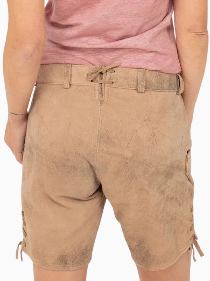 Back view of beige traditional alpine lederhosen-style shorts with a suede-like textured finish, adjustable back lace detail, and side lacing, worn with a pink top.