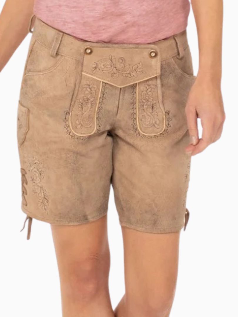 Beige traditional alpine lederhosen-style shorts featuring embroidered detailing and a decorative front flap, worn with a pink top.