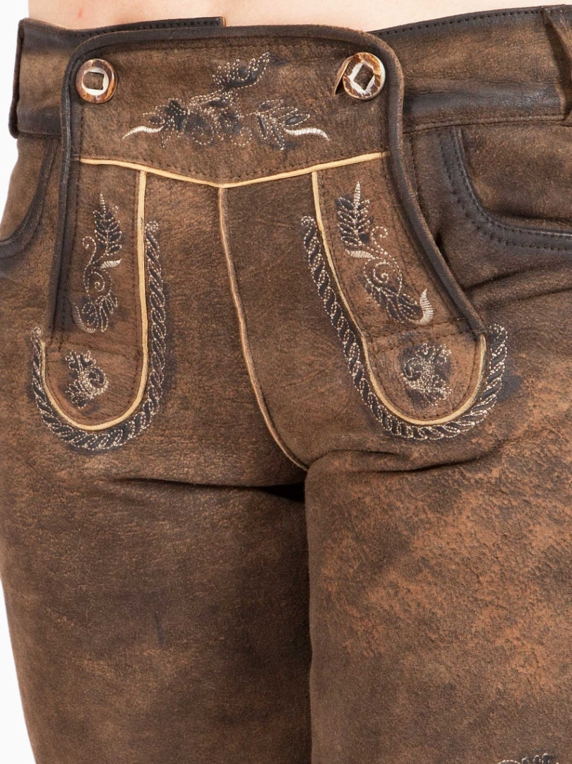 Angled front view of rustic brown traditional lederhosen-style shorts with embroidered detailing, decorative front flap with buttons, and a worn leather texture.