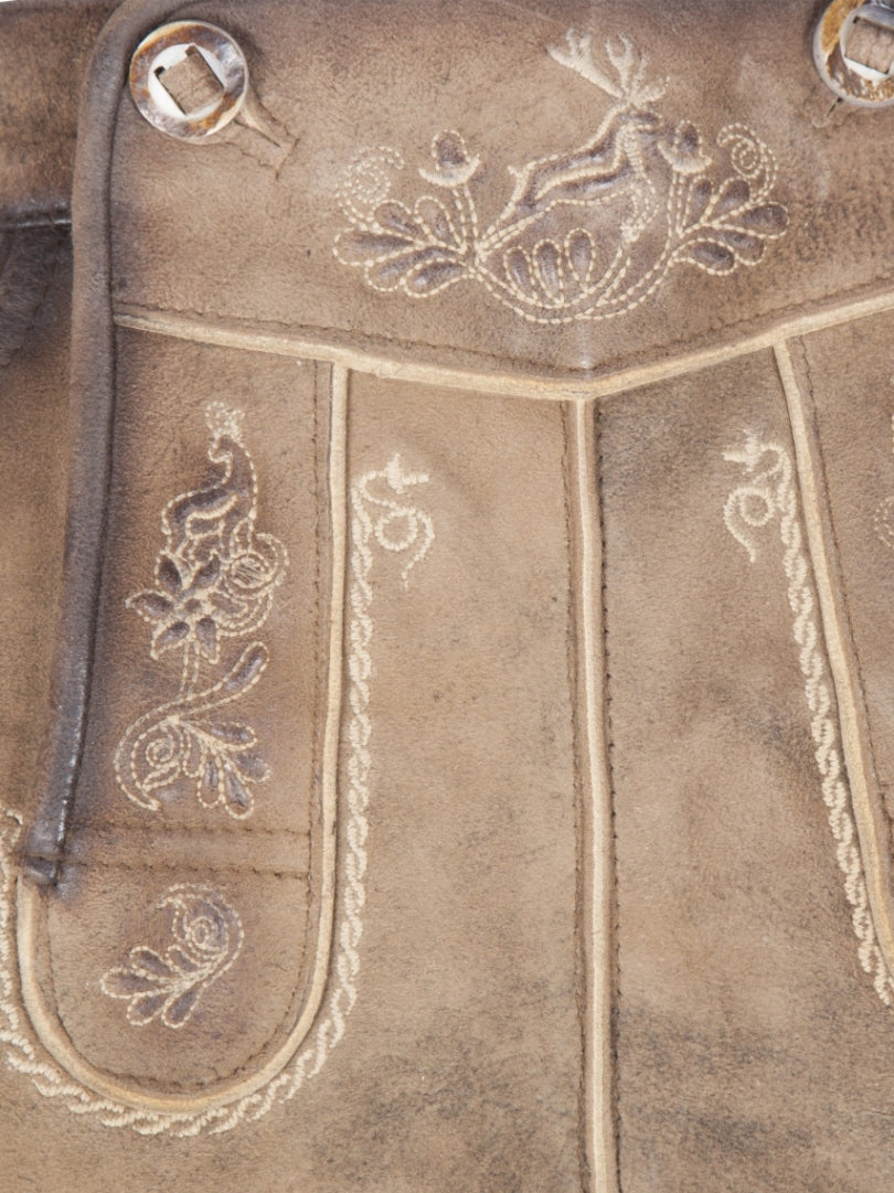 Close-up front detail of traditional lederhosen shorts featuring embroidered deer motif, decorative stitching, and textured suede leather panels.
